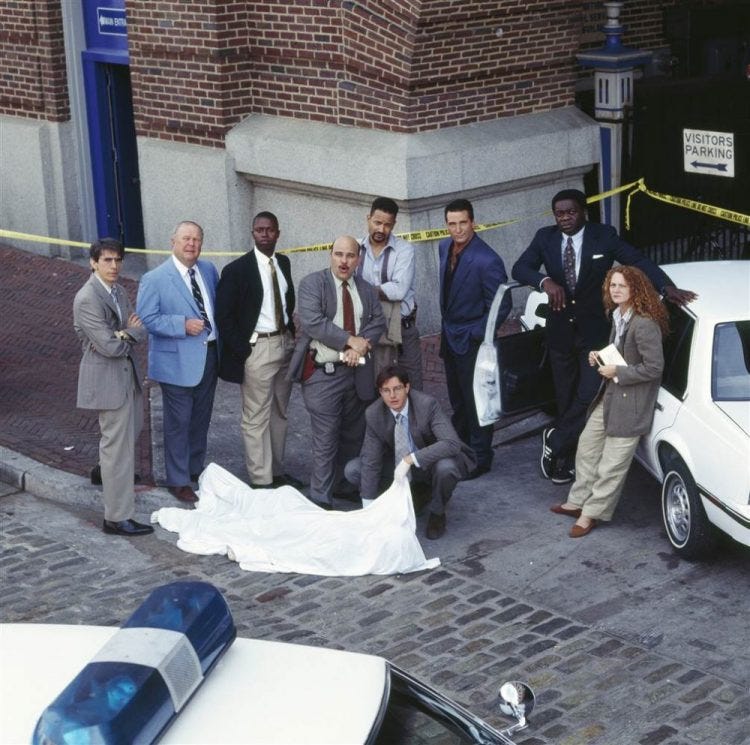 This image shows the principal cast members of Homicide: Life on the Street’s first two seasons posing outside the Baltimore Pier building that doubled as their squad room’s exterior. Left to Right: Richard Belzer (as John Munch), Ned Beatty (as Stanley Bolander), Andre Braugher (as Frank Pembleton), Jon Polito (as Steve Crosetti), Kyle Secor (as Tim Bayliss, kneeling), Clark Johnson (as Meldrick Lewis), Daniel Baldwin (as Beau Felton), Yaphet Kotto (as Al “Gee” Giardello), & Melissa Leo (as Kay Howard). This image shows the principal cast members of Homicide: Life on the Street’s first two seasons posing outside the Baltimore Pier building that doubled as their squad room’s exterior. Left to Right: Richard Belzer (as John Munch), Ned Beatty (as Stanley Bolander), Andre Braugher (as Frank Pembleton), Jon Polito (as Steve Crosetti), Kyle Secor (as Tim Bayliss, kneeling), Clark Johnson (as Meldrick Lewis), Daniel Baldwin (as Beau Felton), Yaphet Kotto (as Al “Gee” Giardello), & Melissa Leo (as Kay Howard).