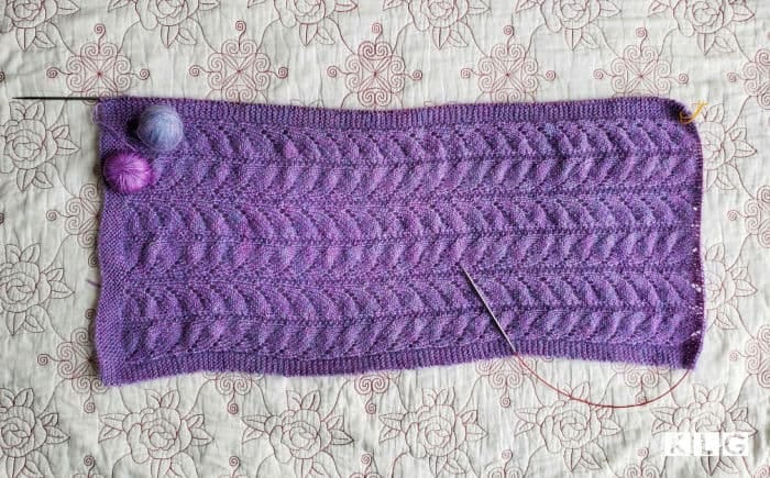 Chasing Light shawl in purple yarns. Lace section with picked up stitches on the long side. Garter stitch section has begun.