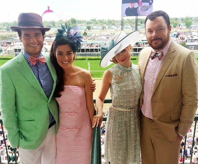 Photo of four people in front of race track wearing loud Kentucky Derby suits, dresses, hats