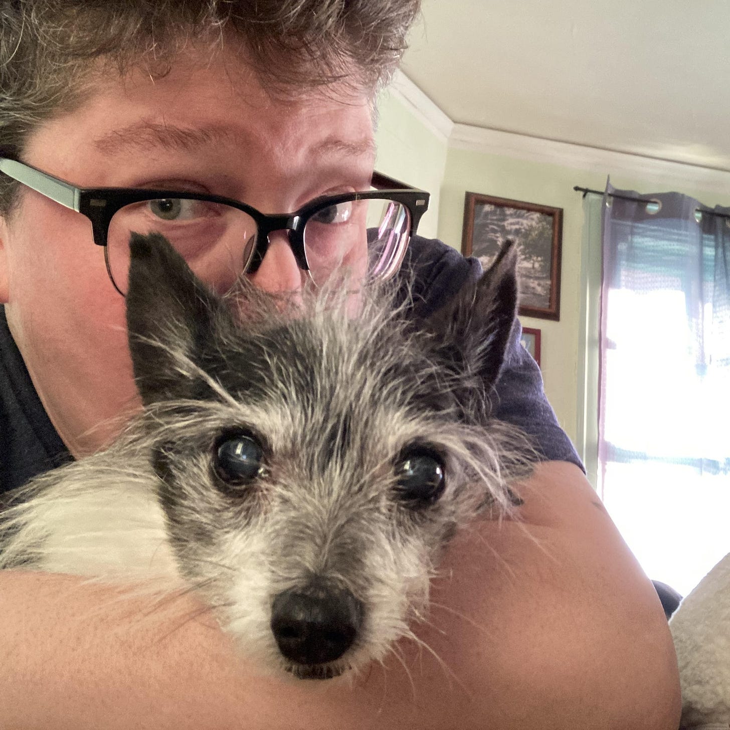 nonbinary person with glasses holding a small black and white dog.