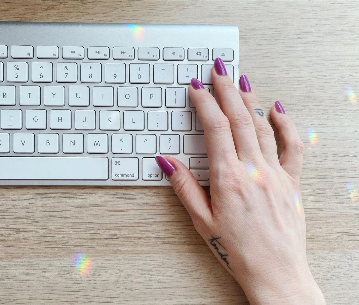 Kate's hand typing on a computer. She has a tattoo of the word tender on her hand