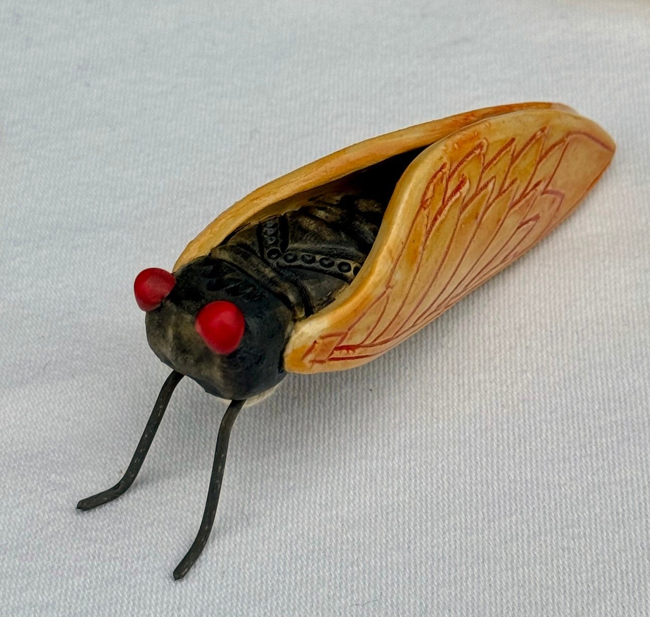 A crappy cellphone snap of a ceramic cicada, with long black front legs, golden wings, and round red eyes