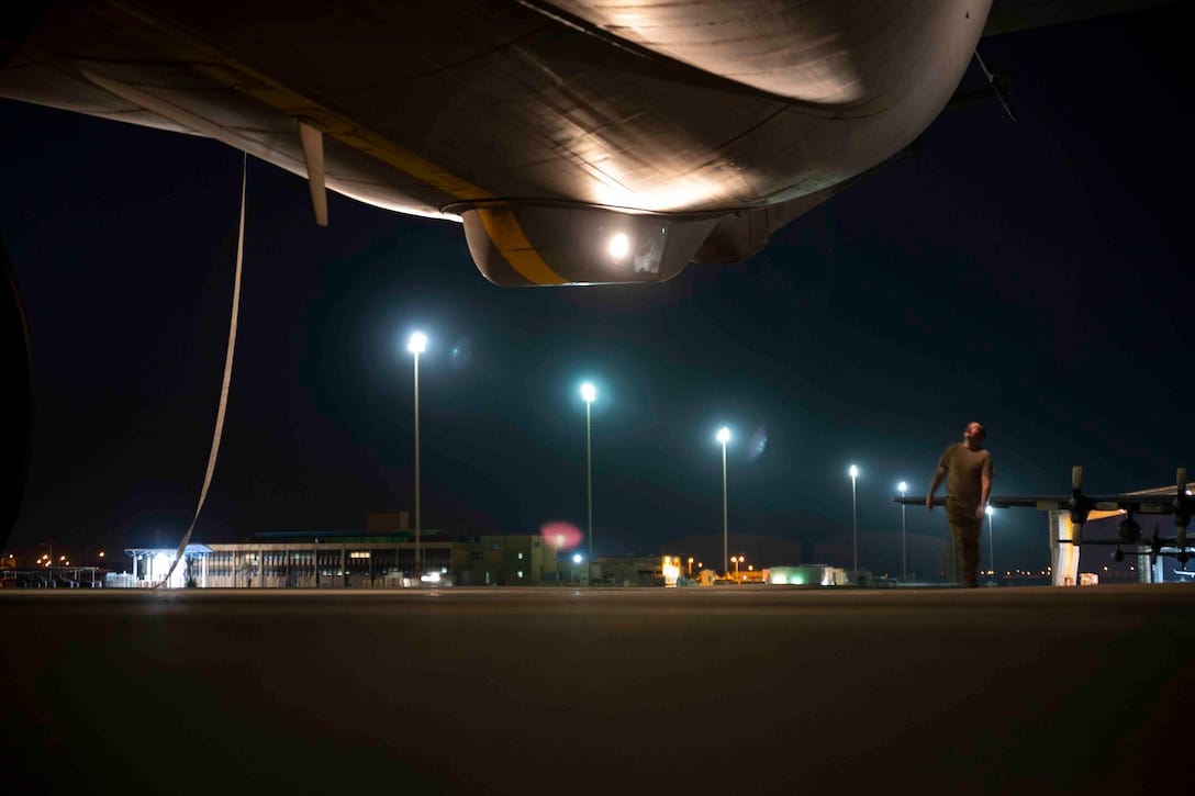 An airman looks underneath a parked aircraft at night.