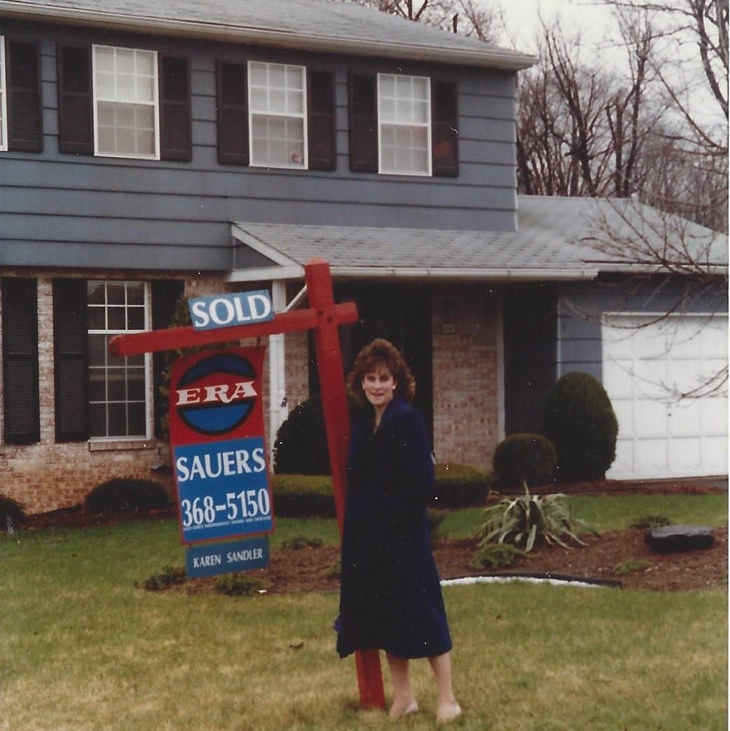 Young woman standing proudly alongside the "for sale" sign of the house she just purchased