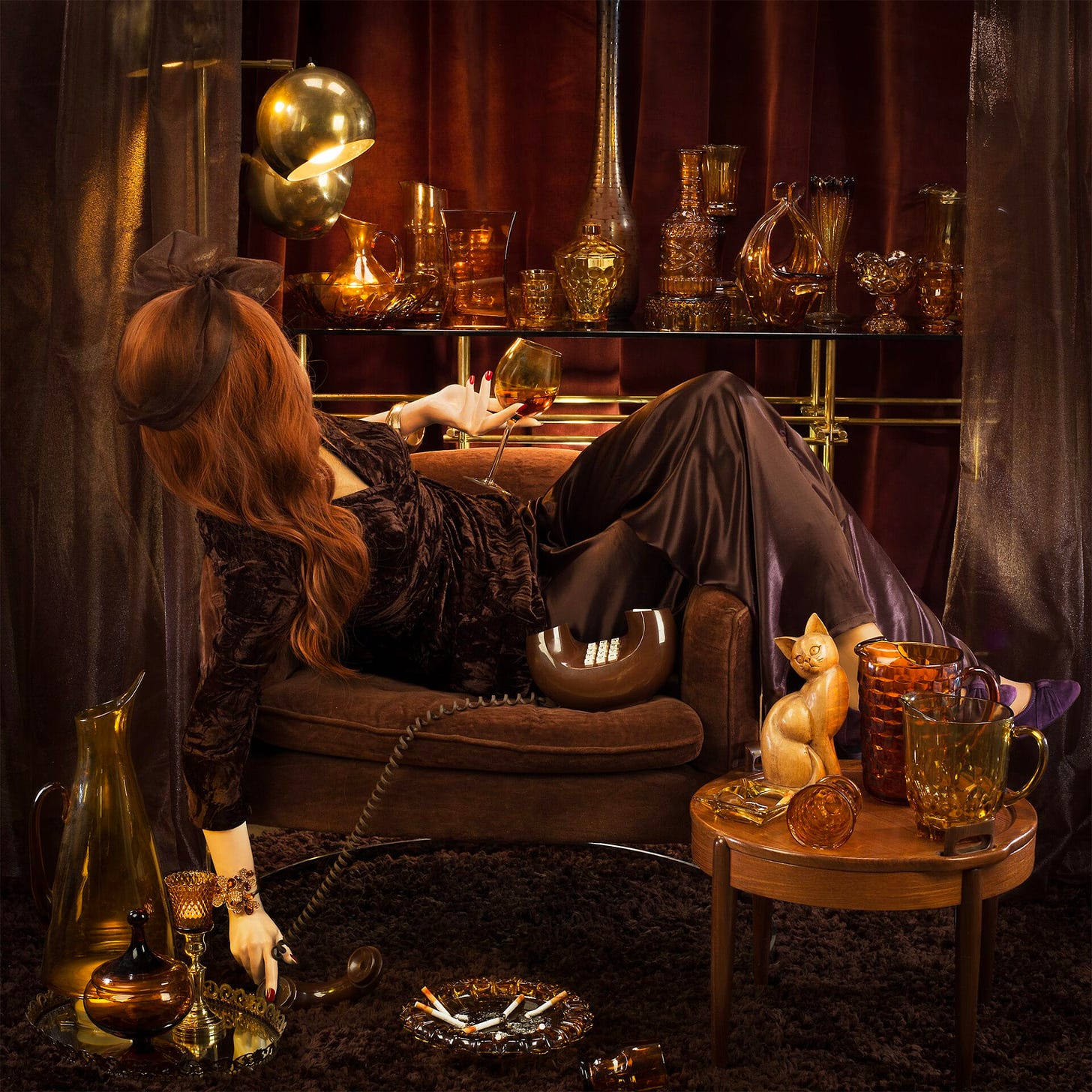 an elaborately staged photograph with a brown theme featuring a posed mannequin sprawled over a chair with a brown donut phone and overwhelmed by a chaotic scene of smoky brown glassware