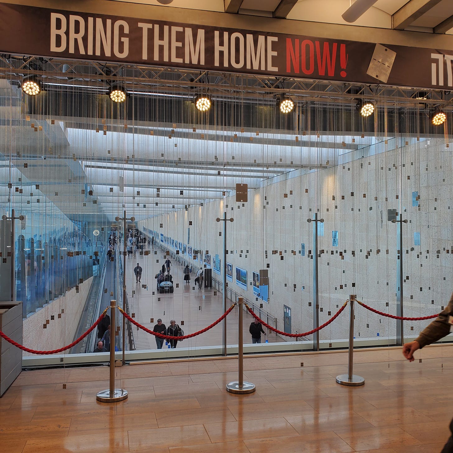 Hundreds of dog tags hang under a sign that reads "Bring Them Home Now" in English and Hebrew. 