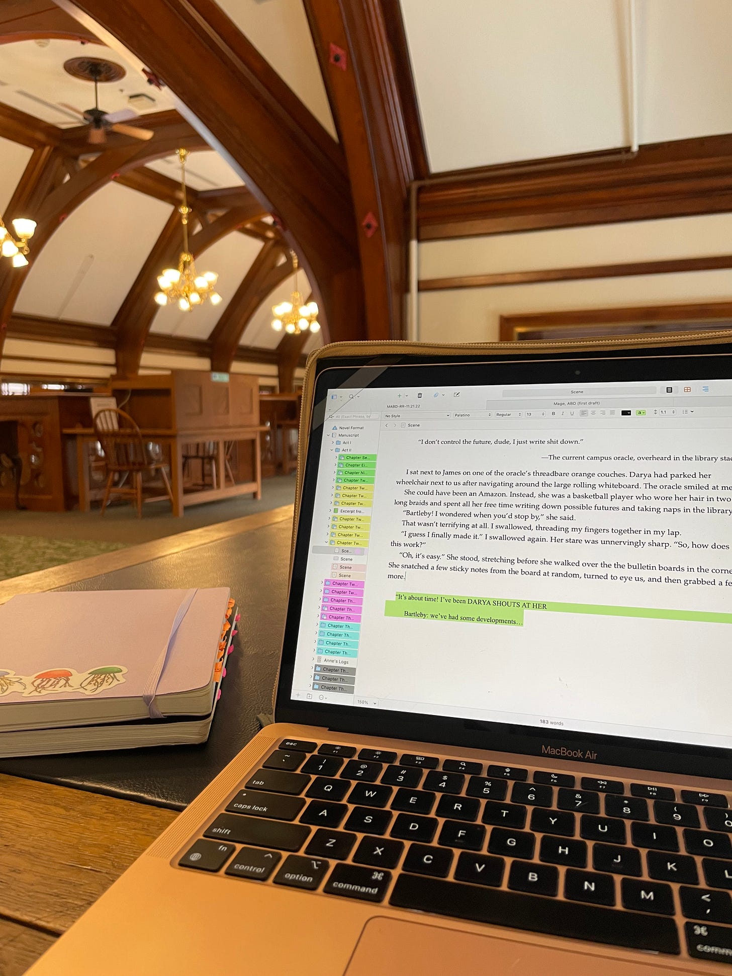 My laptop with color-coded scrivener project open. In the background, a beautiful library with chandeliers. 