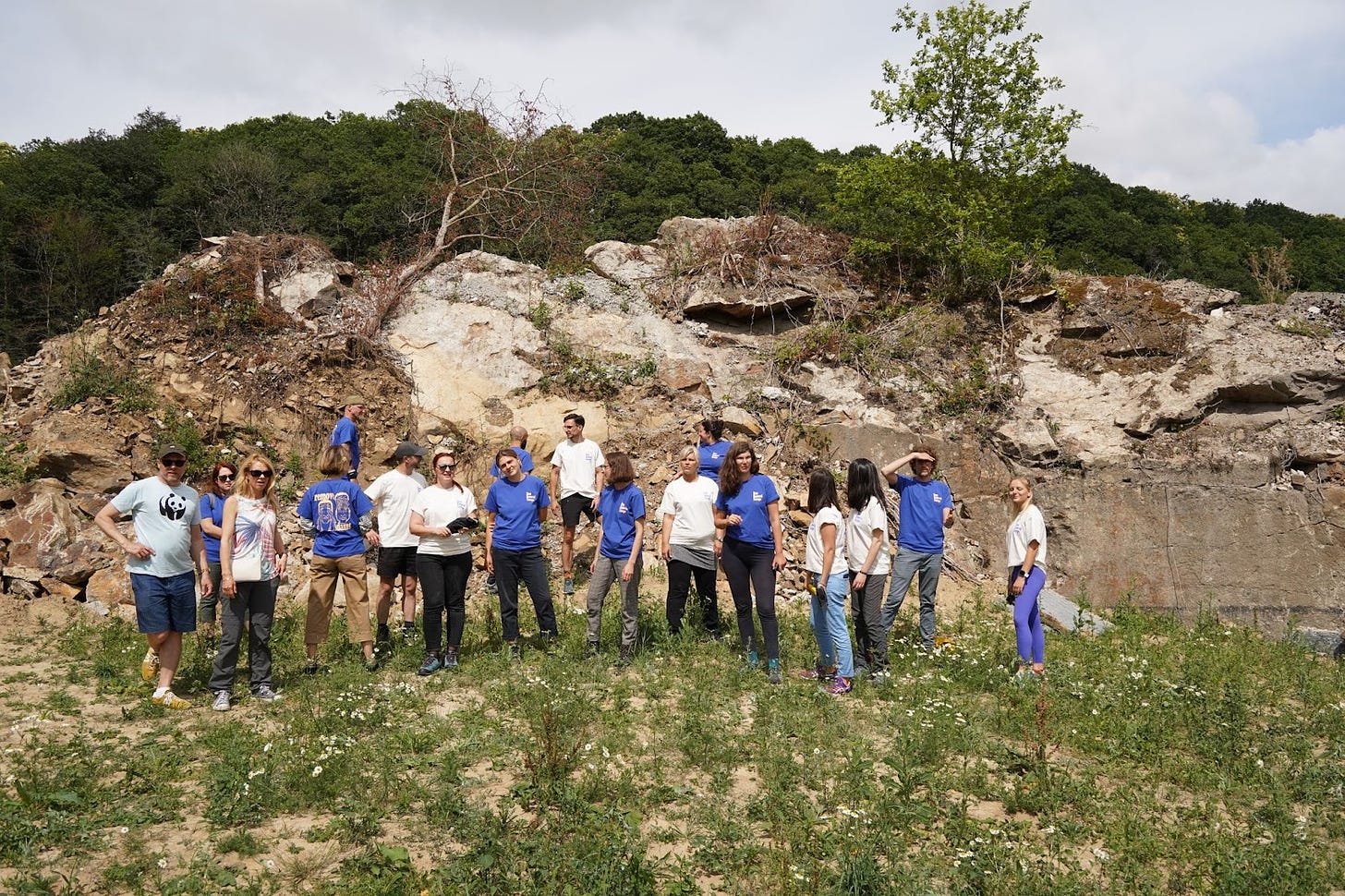 A group of people stand in a wooded area by an old dam in blue and white shirts