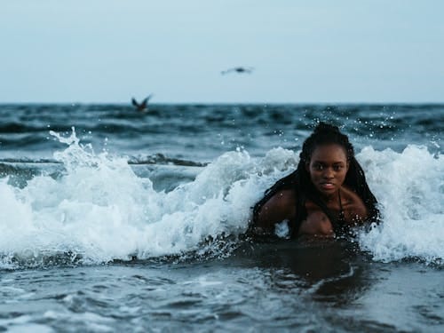 Free African American woman playing in ocean waves during summer vacation. Stock Photo