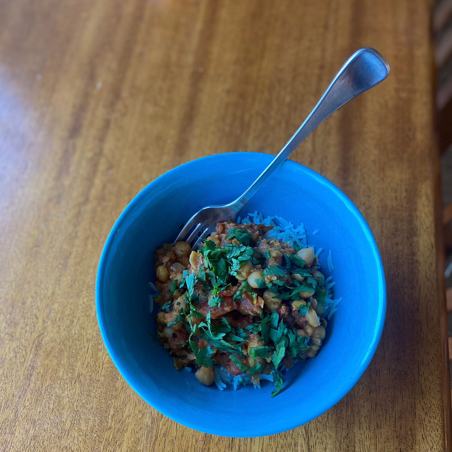 In a blue bowl, the chana masala described above, covered with chopped cilantro and served over basmati rice.