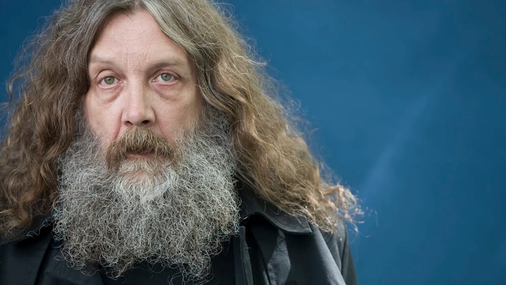 Alan Moore staring at the camera against a blue background