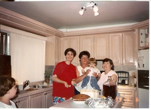 Three women - Cassandra's mom and two grandmothers - hold her up on the counter in front of her cakes. It is her second birthday.