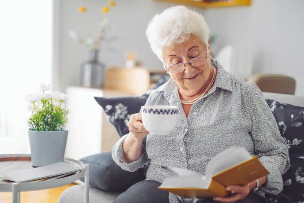 Elderly Woman reading a book with a cup of tea