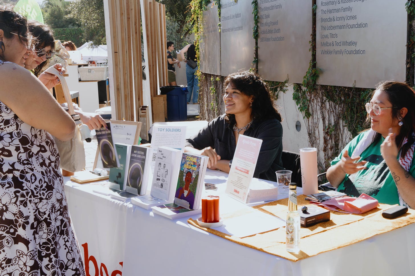 Abode founder Diamond Braxton and Poetry Editor SG Huerta tabling at front market, selling a copy of My Sisters Look Like God