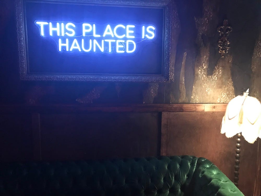 Creepy dark room lit by a single lamp with "This place is haunted" neon sign