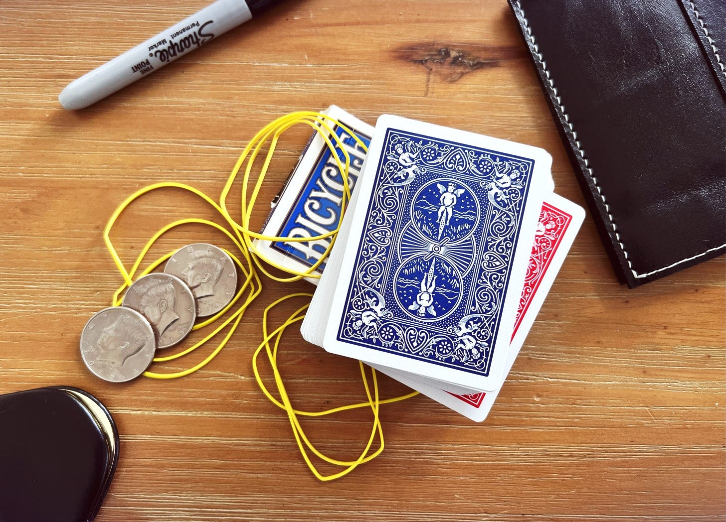 A table with deck of cards, rubber bands, coins, sharpies and a wallet
