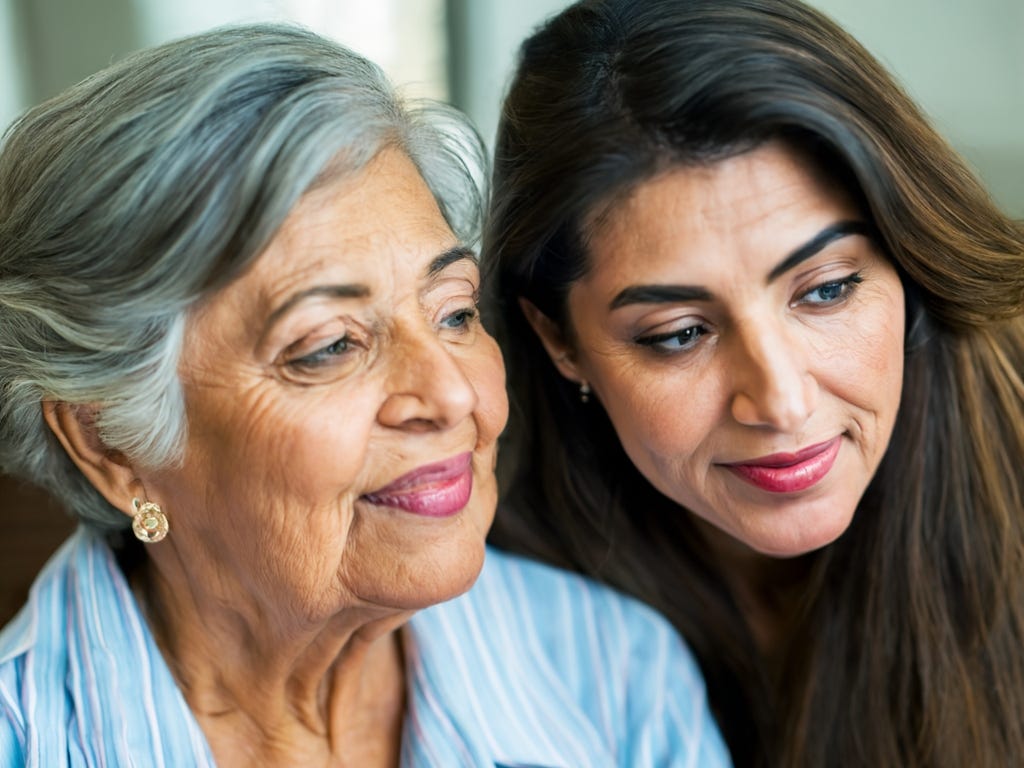 Two pensive-looking women, one much older (at 84 years old) with short gray hair and the other just 35 years old with long black hair, close together and looking off camera.