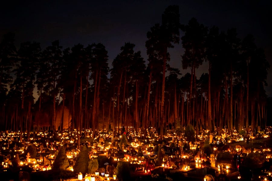 Hundreds of candles and lanterns illuminate graves in a cemetery.