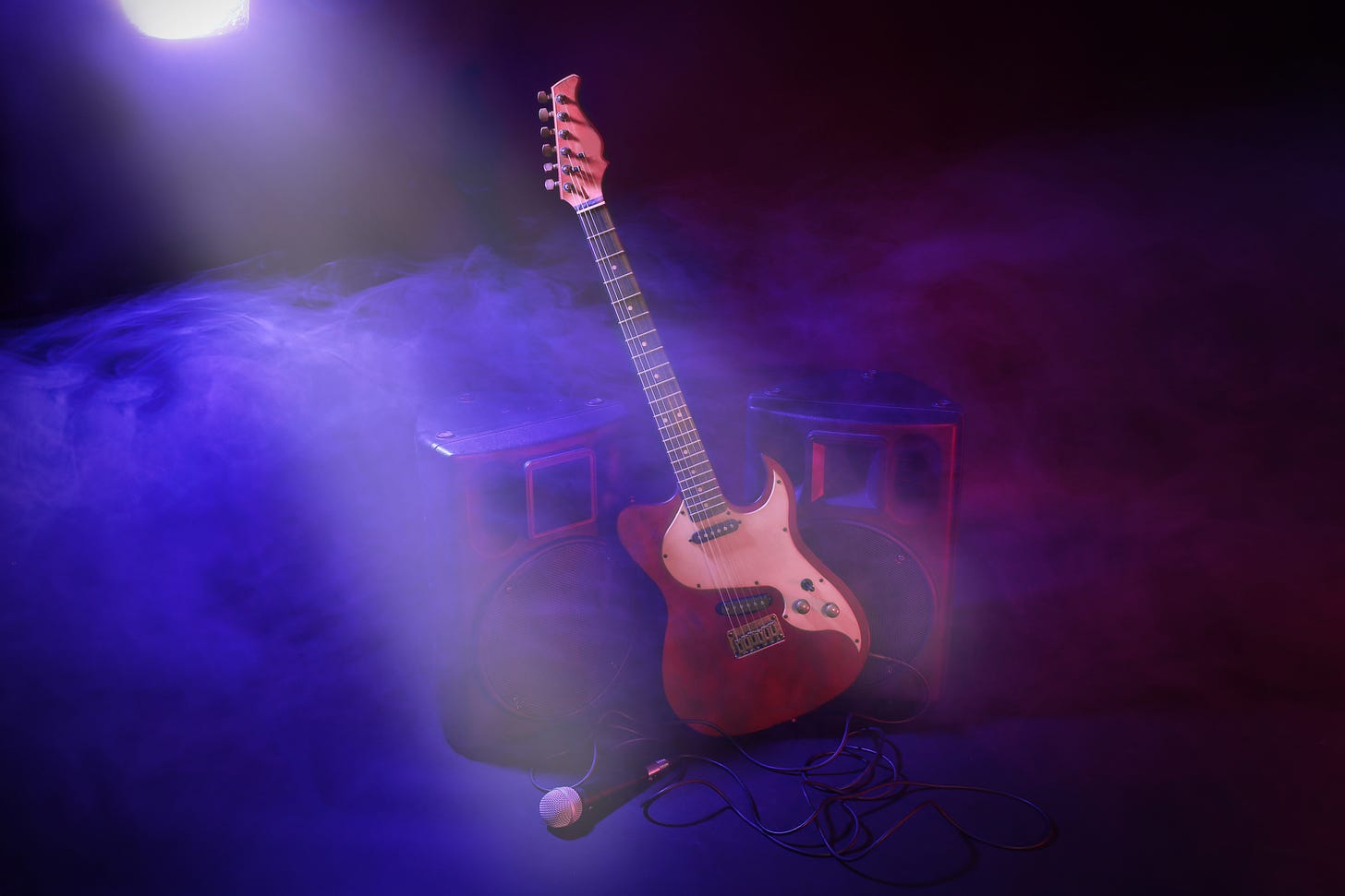 Electric guitar propped against speakers with mic on floor of a dark stage with purple smoke