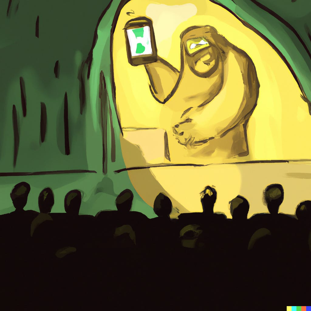 A big yellow character on stage holds up a mobile phone in front of a silhouetted audience.