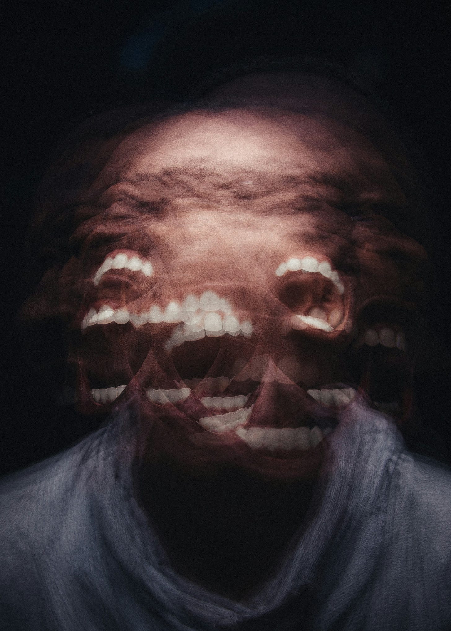 multiple overlayed transparencies of a male screaming wildly, bearing teeth, shaking his head side to side.