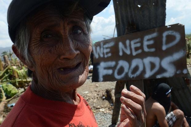 A victim of devastating Typhoon Bopha begs for alms next to a sign displayed along the roadside in the town of Nabunturan town in Compostela Valley province on Sunday. Photo: AFP (AFP )