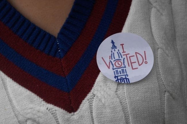 A person in a red, white and blue sweater wears an "I Voted" sticker.