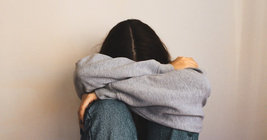 a woman sitting on the floor with her arms wrapped around her head