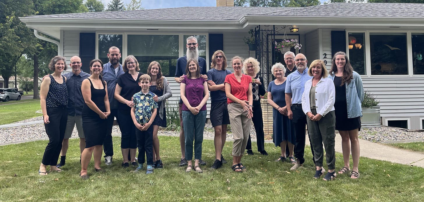 Seventeen people stand in front of a house smiling for the camera