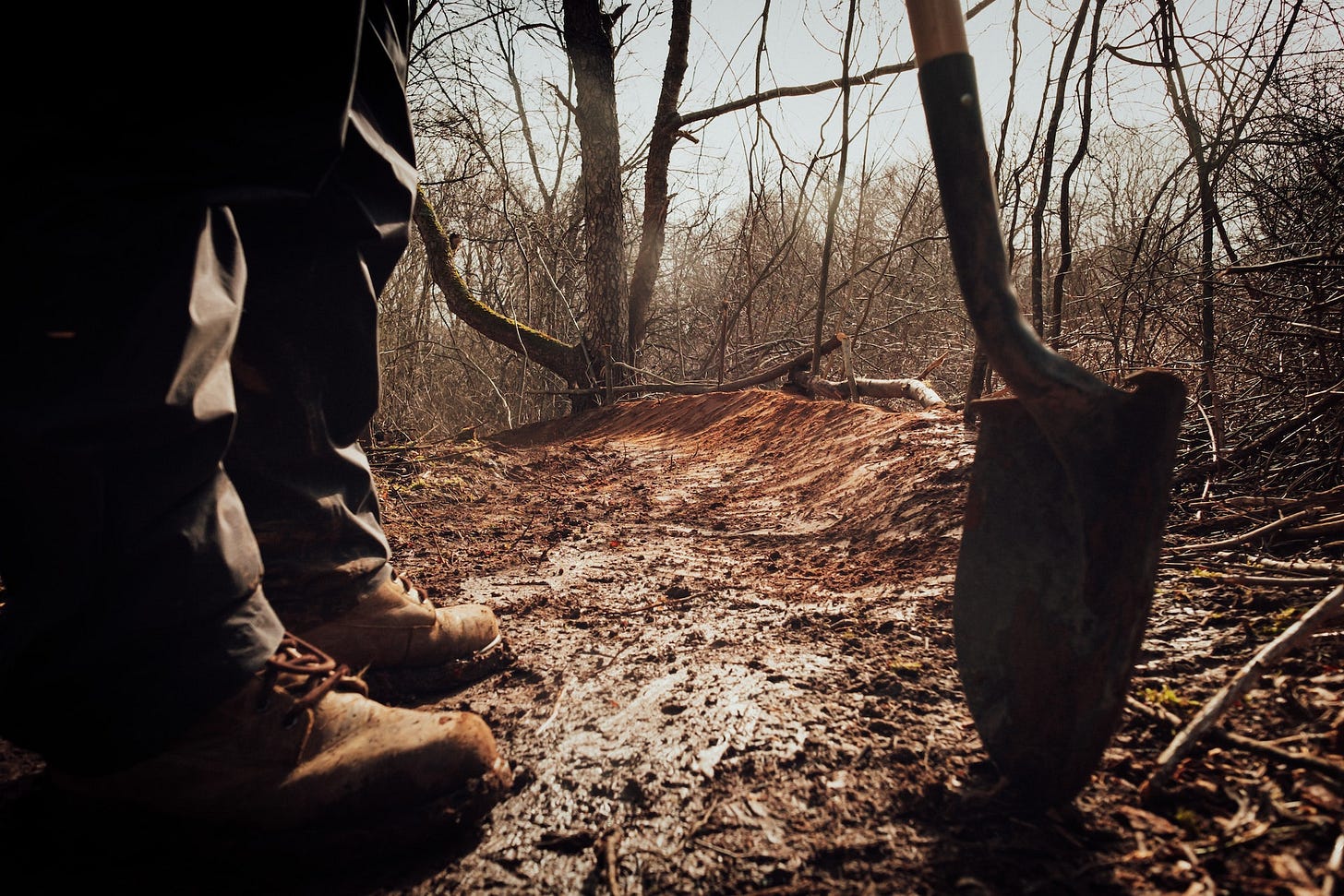 A pair of feet in boots and the tip of a shovel on wooded ground. A pair of feet in boots and the tip of a shovel on wooded ground.