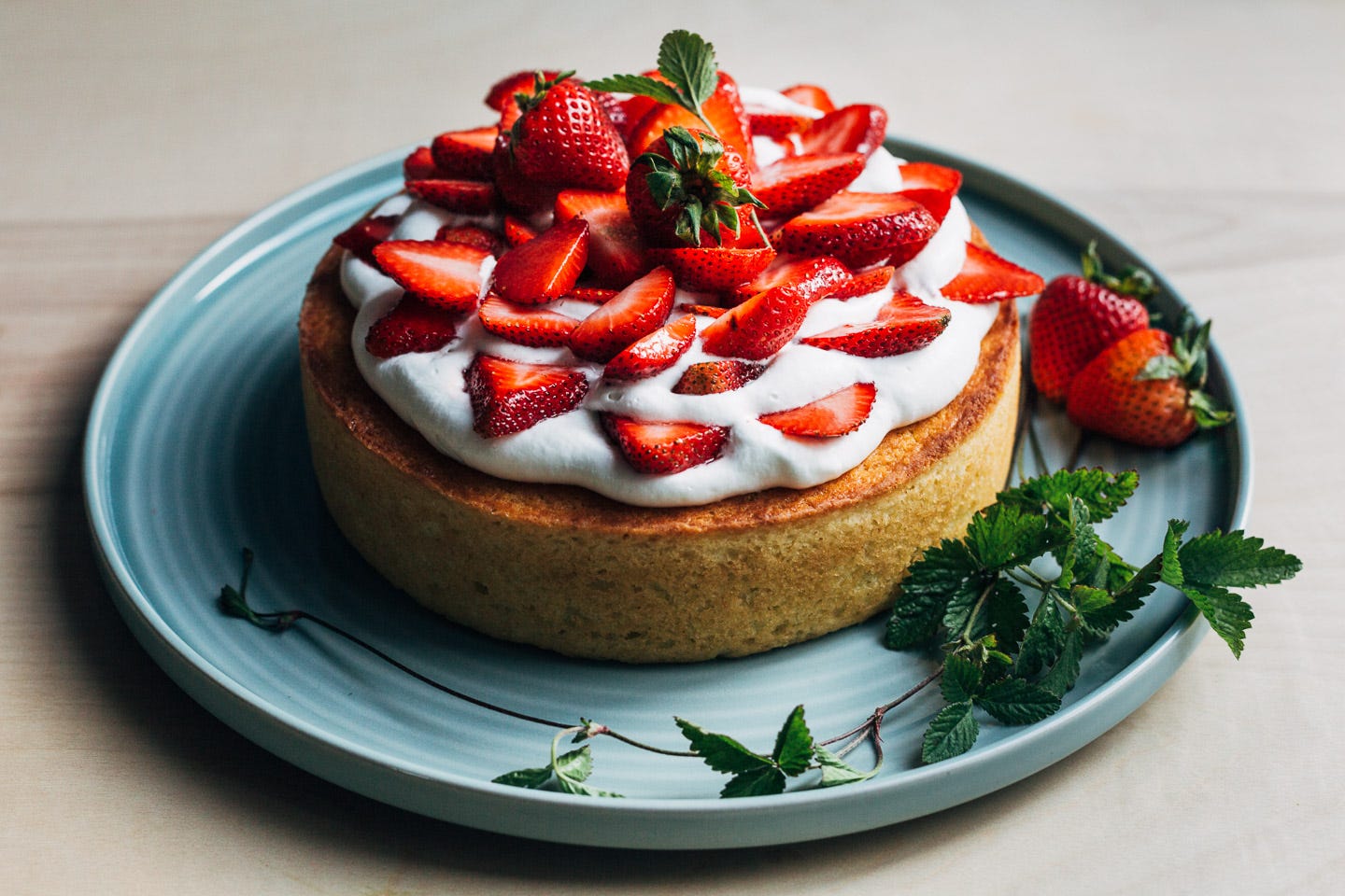 A cake ready to serve, with strawberries and whipped cream on top, and whole berry and strawberry leaf garnishes. 