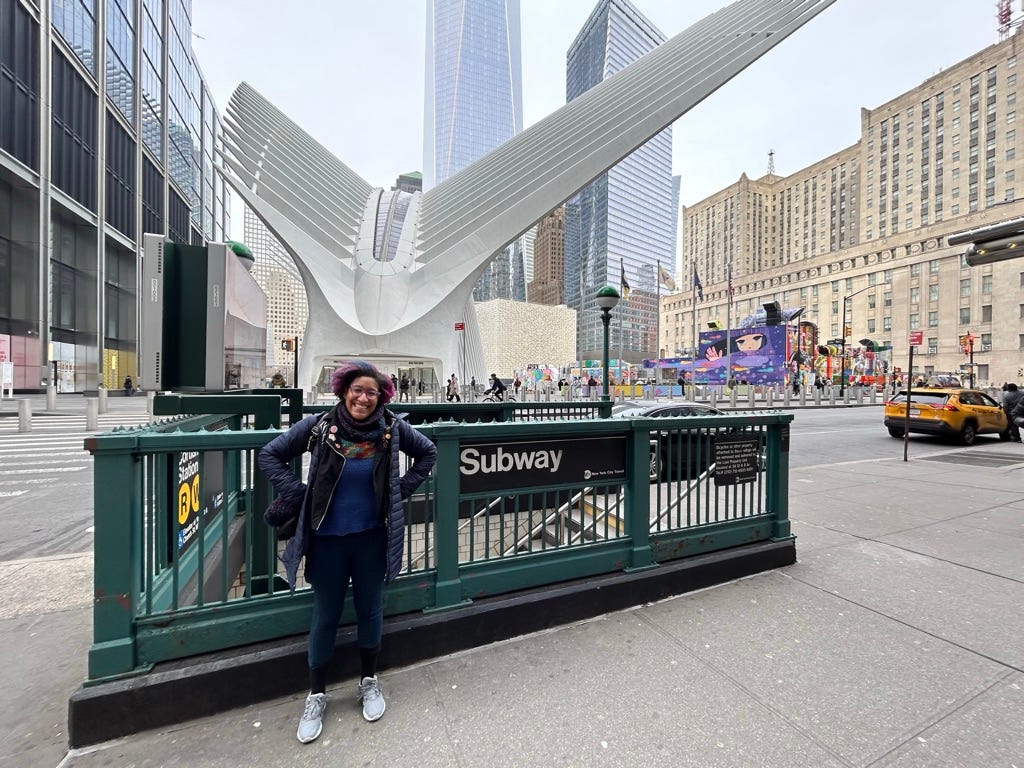  Kristen stands in her puffy winter coat and her cotton “motorcycle” jacket in front of a green subway entrance to the R&W lines across the street from the Occulus and the 9/11 Memorial.