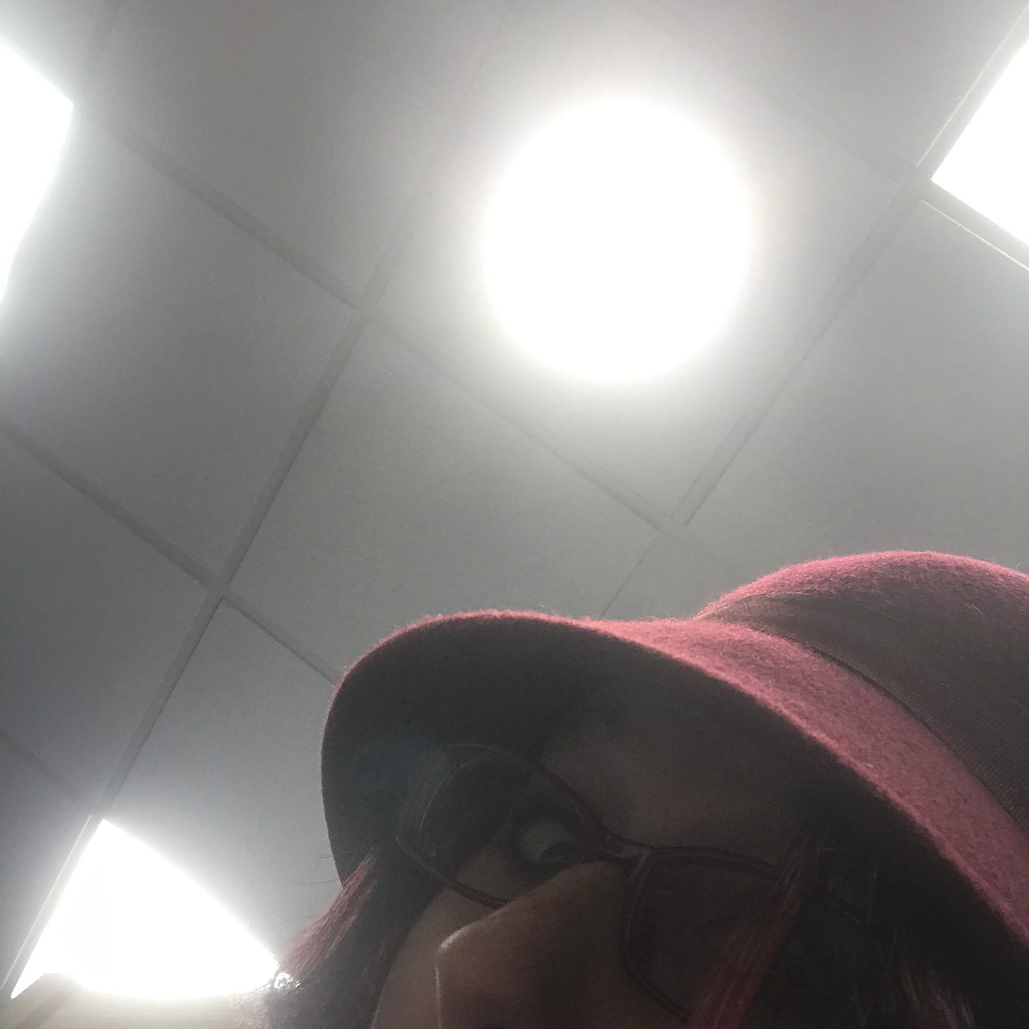 Image of Lyric Rivera, in 2017, taking a selfie with a painfully bright light. They have a red felt had on, shading their face.
