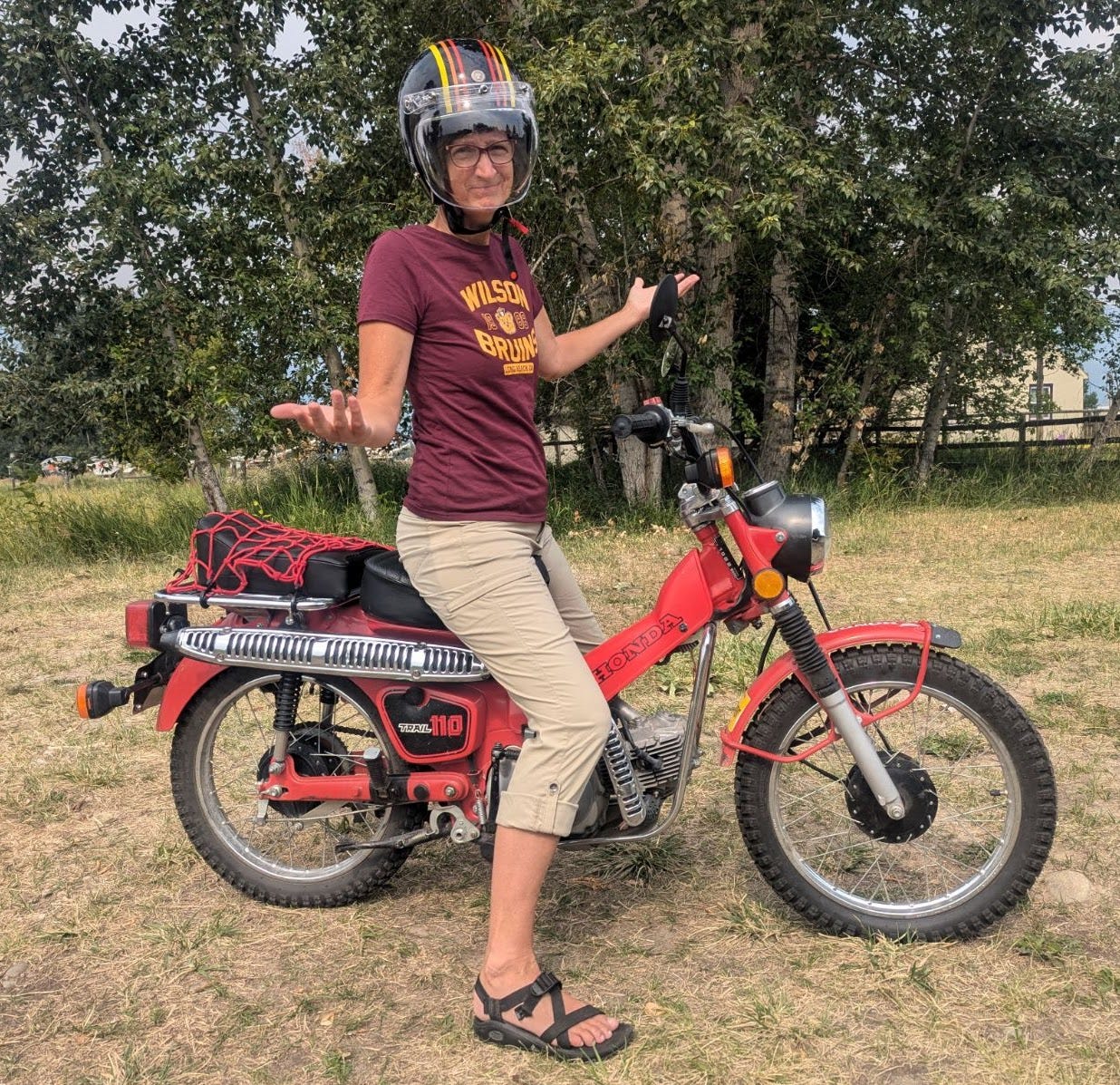 a middle aged woman with a helmet, sitting on a vintage red motorbike, lifting up her hands in frustration