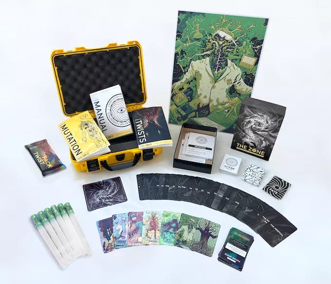 A collection of cards, glowsticks, and a book next to an open industrial case. All laid out on display showing off the contents of the Kickstarter for The Zone.