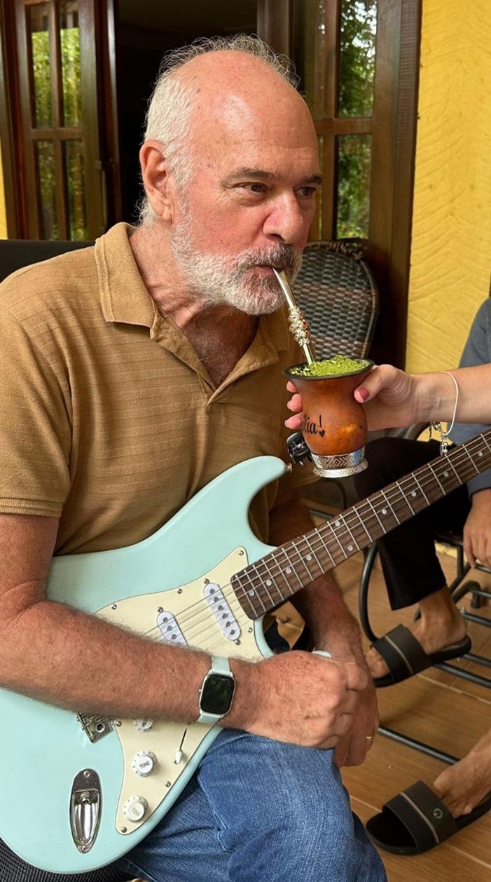 Dr. Sircus, enjoys a mate while holding an electric guitar, showcasing a moment of leisure and creativity.