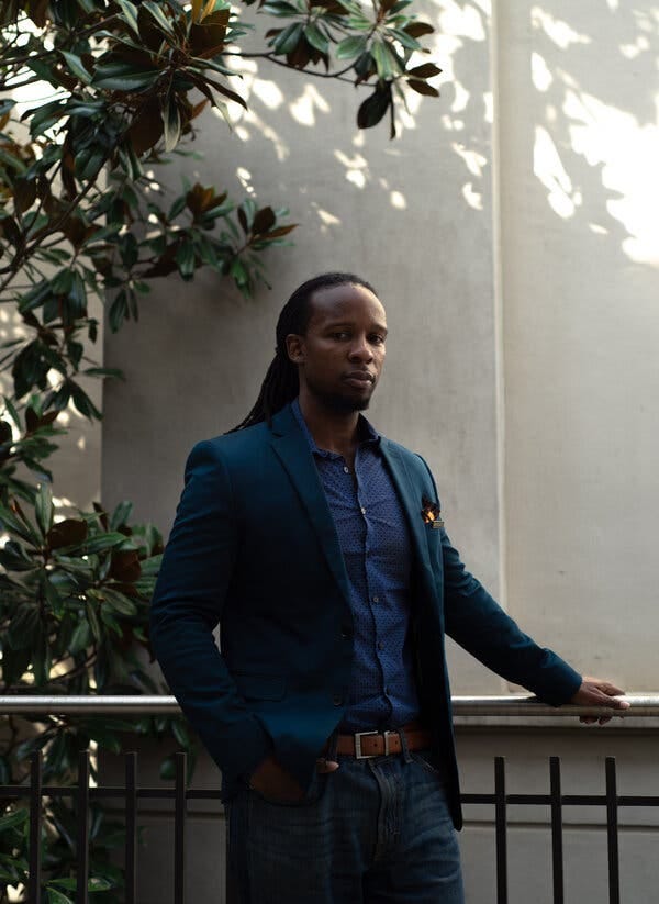 A portrait of Ibram X Kendi, a young man dressed all in blue, standing with his hand on a railing.