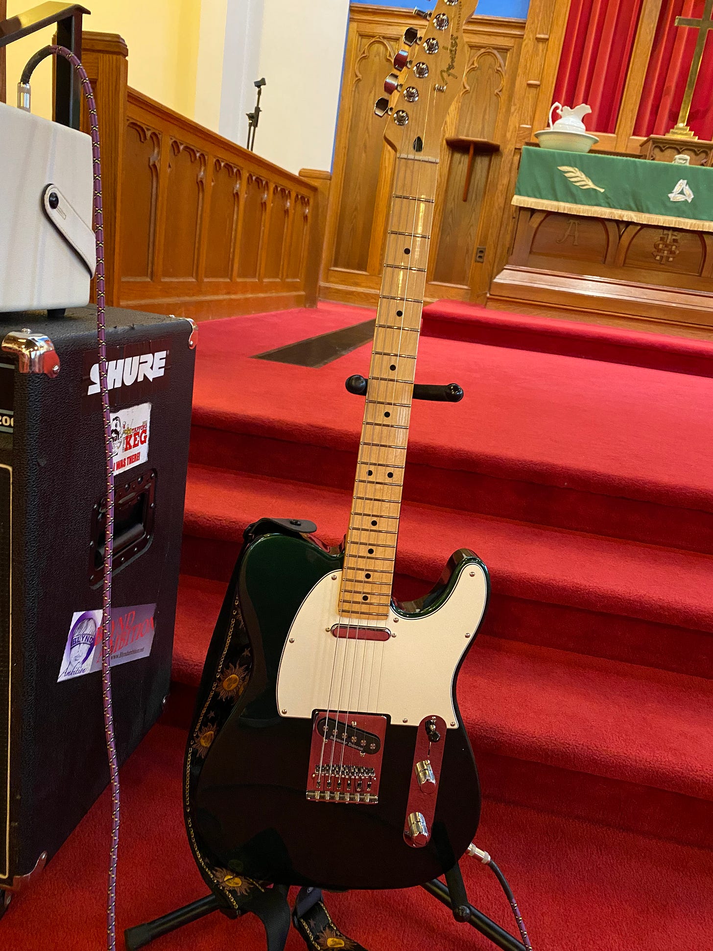 Photo of Fender telecaster sitting on a guitar stand in a traditional, red carpeted church sanctuary