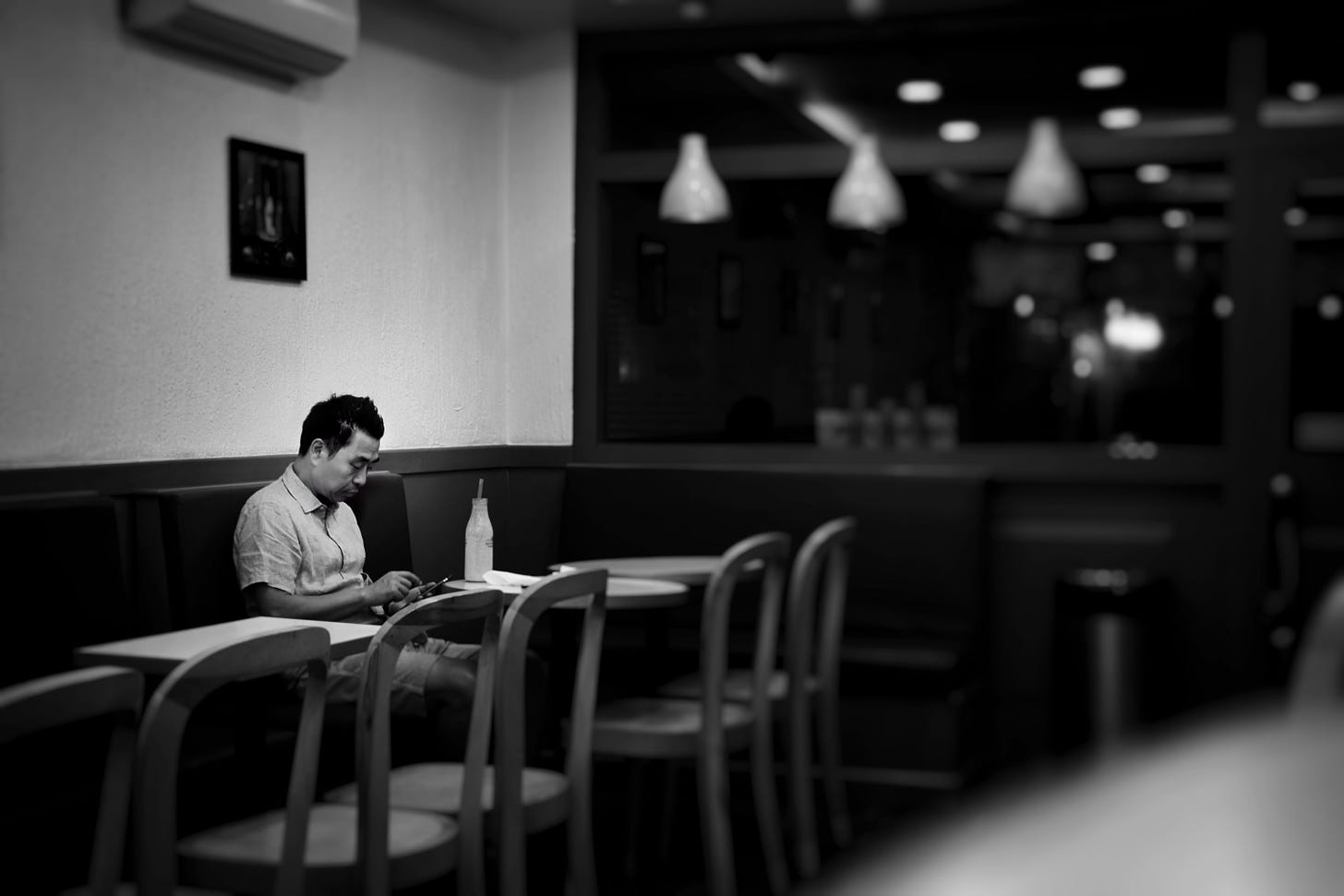 A man sits alone in a restaurant looking down at the table.