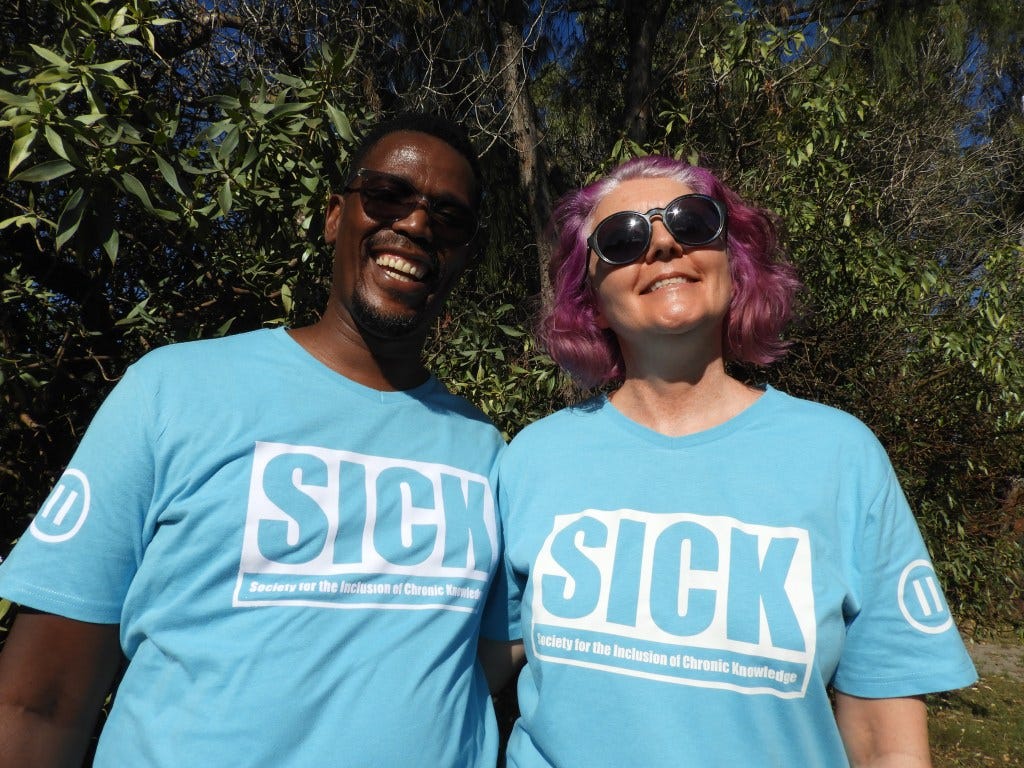 The two advocates smile at the camera, wearing blue and white T-shirts reading "SICK: Society for the Inclusion of Chronic Knowledge"