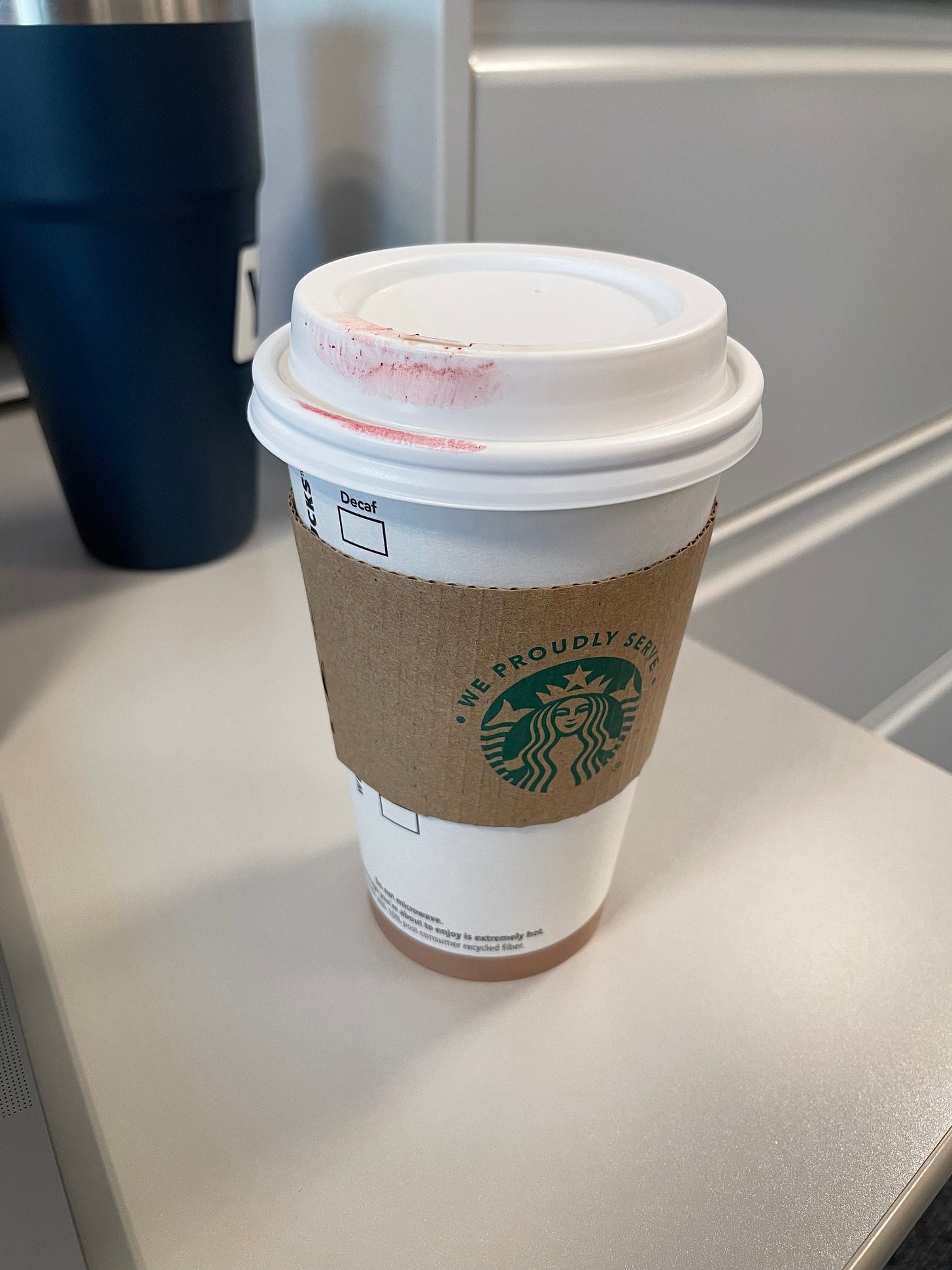 A starbucks cup with a lipstick stain sits on a desktop. 