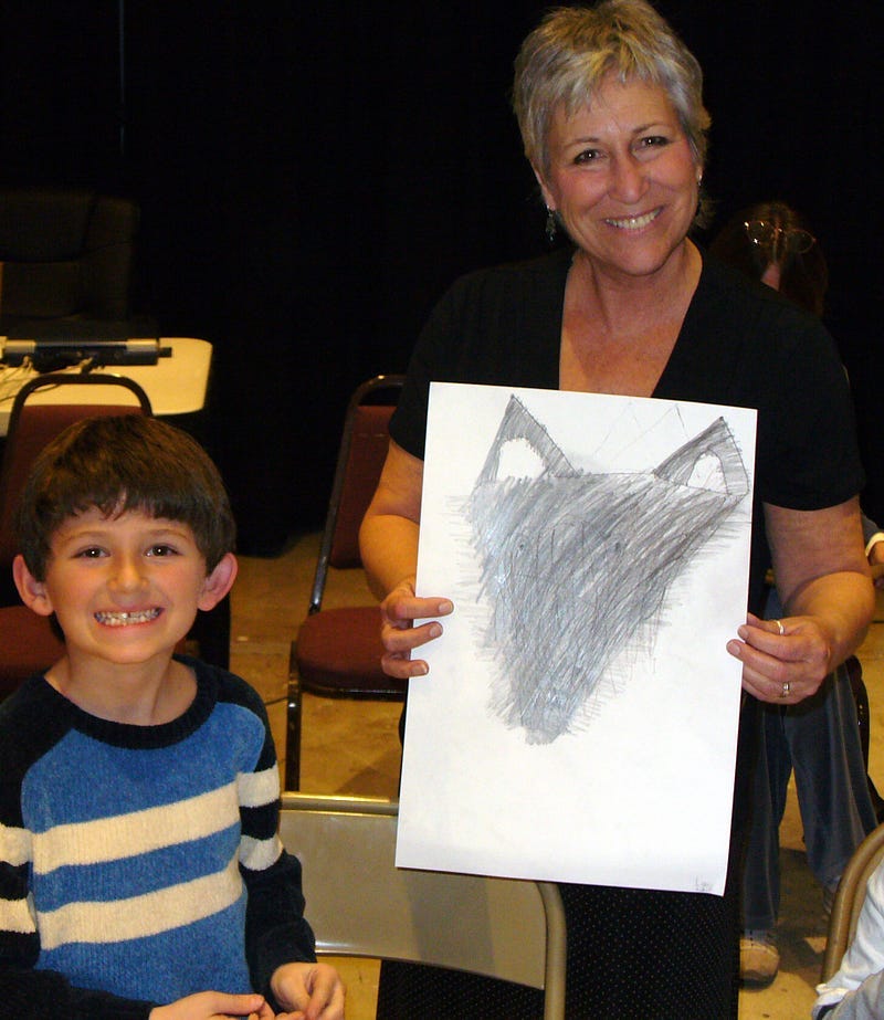 Photo of artist Sherry Killam with a student and completed artwork of a wolf portrait.