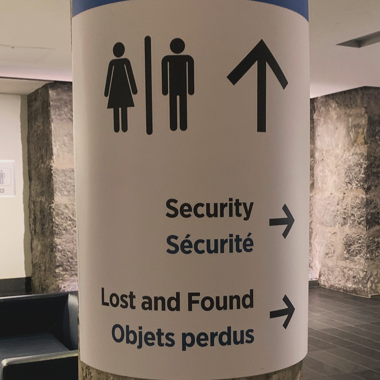 A direction sign on a pillar, in French and English, with directions to the bathroom, scurity, and Lost and found
