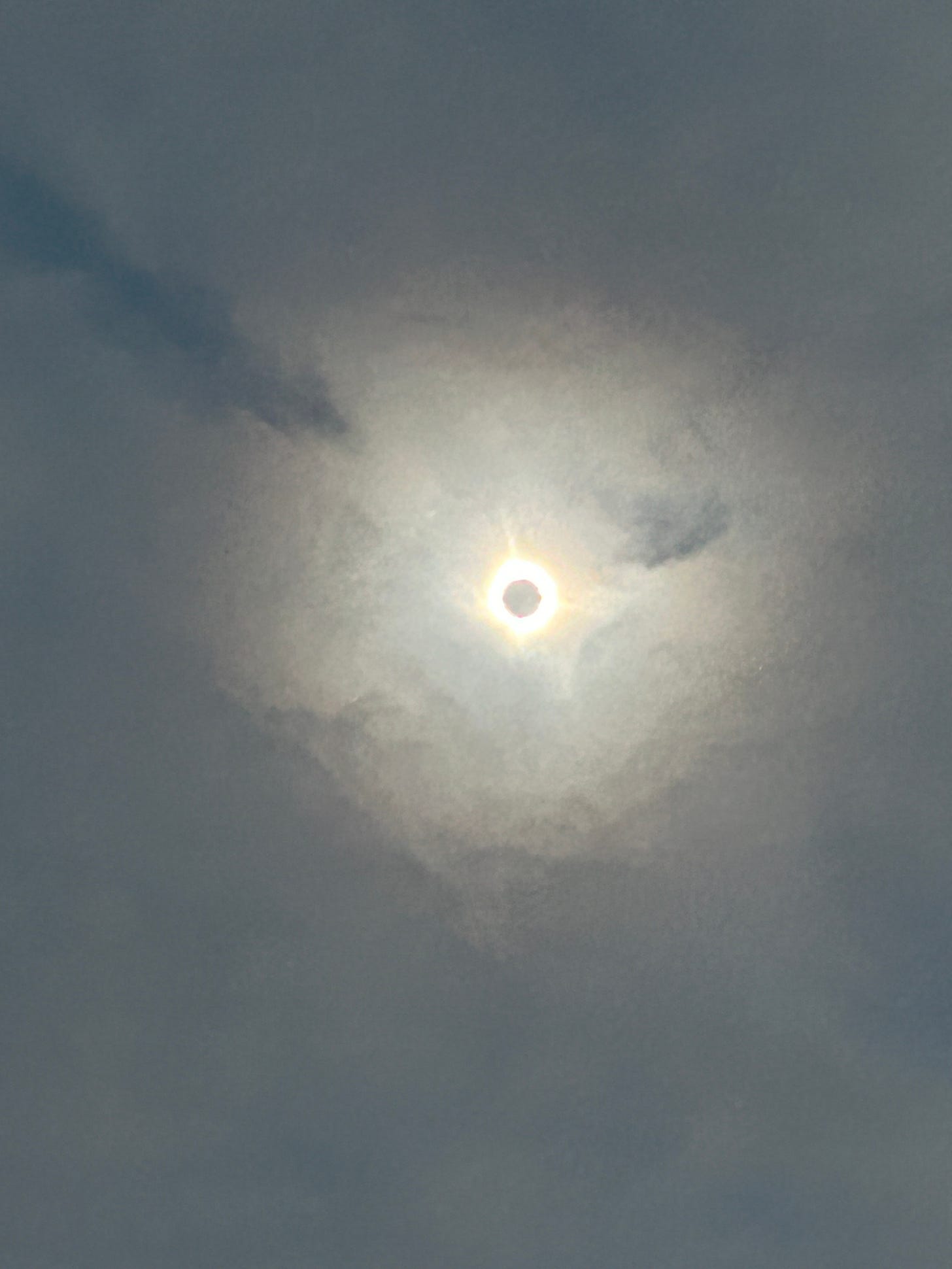 The moon appears in a cloudy sky as a dark circle over the bright disk of the sun. 