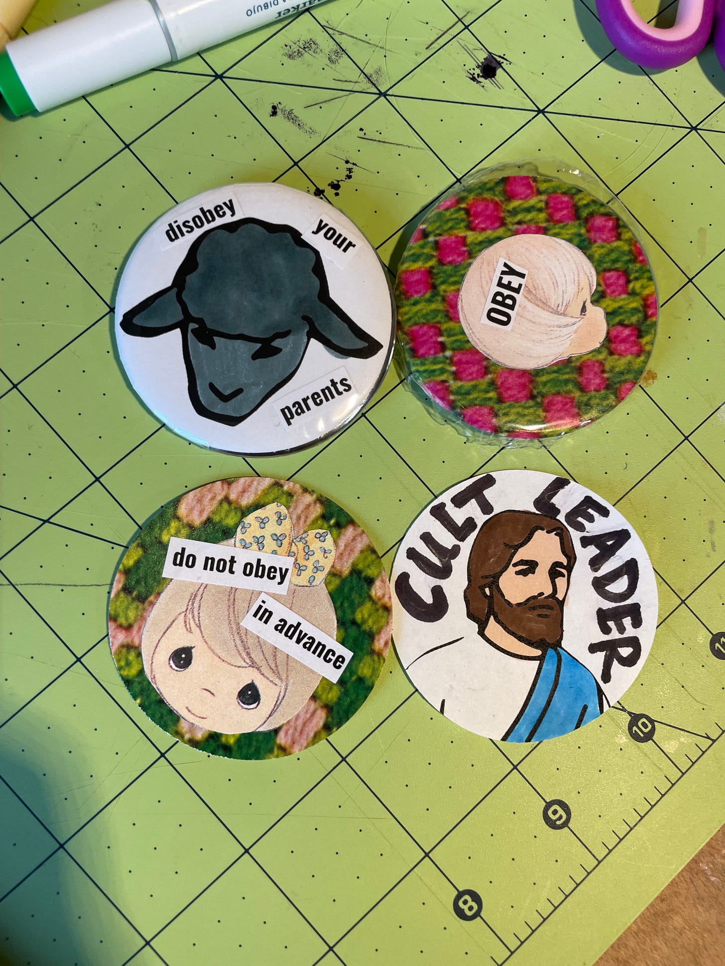 four large buttons on a messy workstation. one is a drawing of a black sheep that says disobey your parents. another is a precious moments child with the word obey in their head. Another is a precious moments face that says do not obey in advance. Another is of a cartoon drawing of Jesus that says cult leader