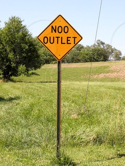 a cheap photoshop of a stock image of a road sign in a grassy field, reading "noo outlet"