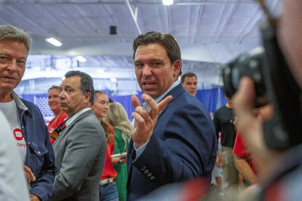 Gov. Ron DeSantis speaking with supporters at a gathering. Several people are visible behind him. 