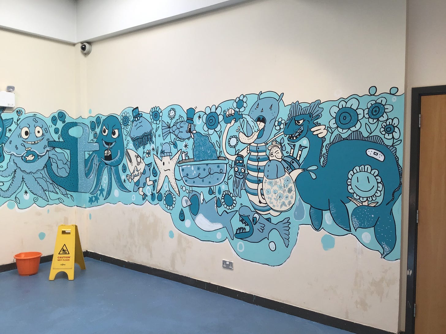 A mural on an interior library wall depicts cartoonish sea creatures and ocean life in a multitude of shades of blue and white paint.