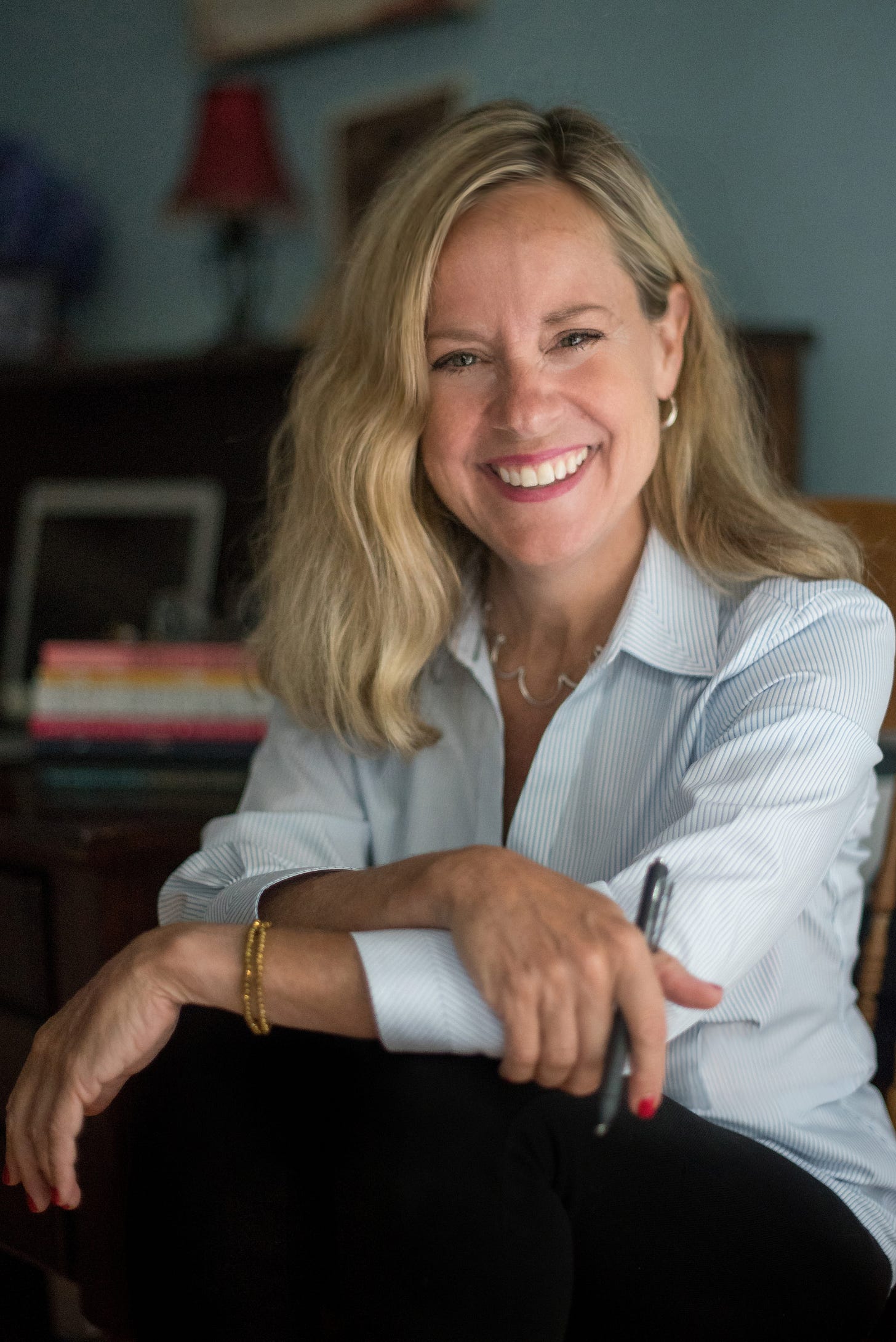 Blonde woman with shoulder length hair holds a black pen and smiles at the camera