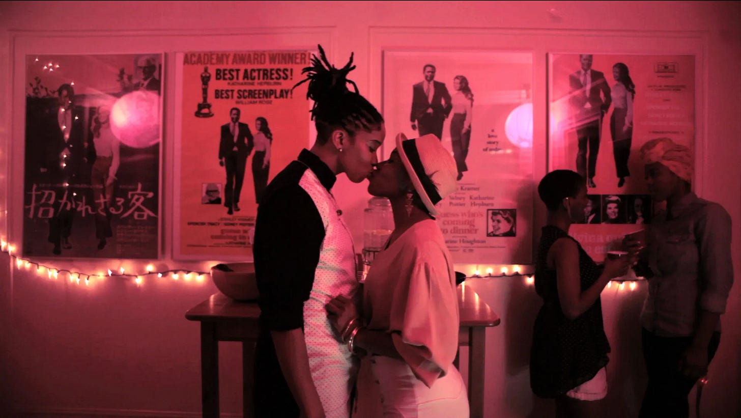 a masculine black lesbian with dreadlocks kissing a feminine black woman wearing a dressy hat in a beautiful house party setting